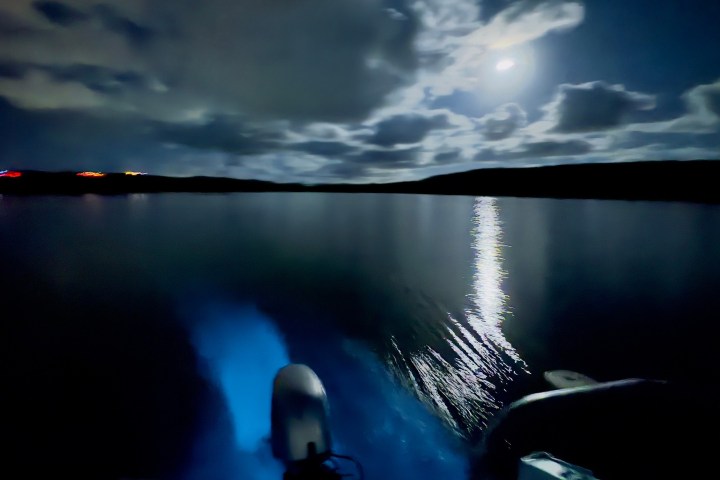 Nighttime lake view with moon reflecting on water and a boat motor visible in the foreground.
