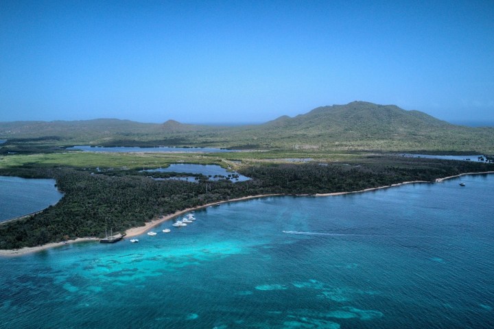 Aerial view of a green island with hills, surrounded by blue ocean.