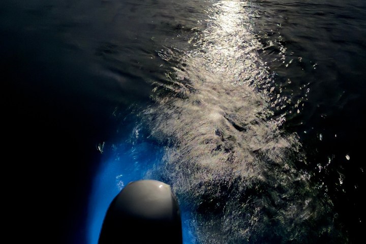 Boat engine with blue light reflecting on water under moonlight.
