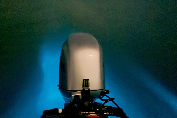 Boat motor at night with glowing water under starry sky.