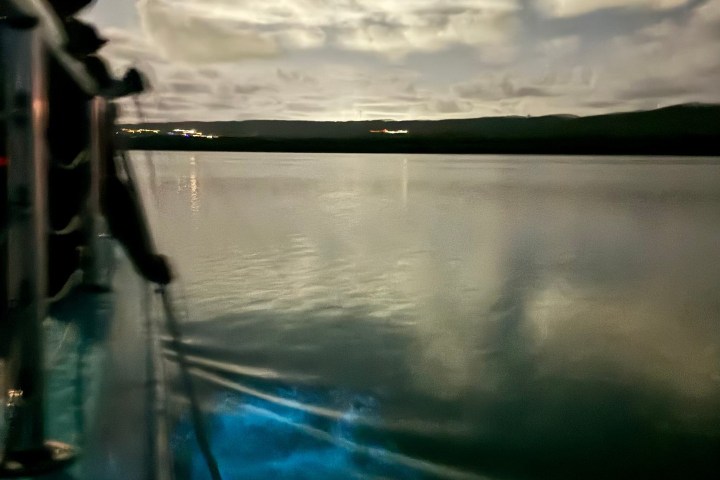Night scene on a boat, glowing water, starry sky, and clouds.